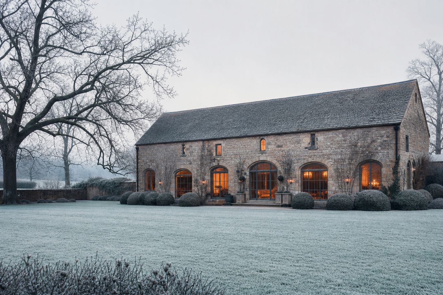 Frosted estate lawn and the candlelit barn glowing warmly on a crisp winter afternoon